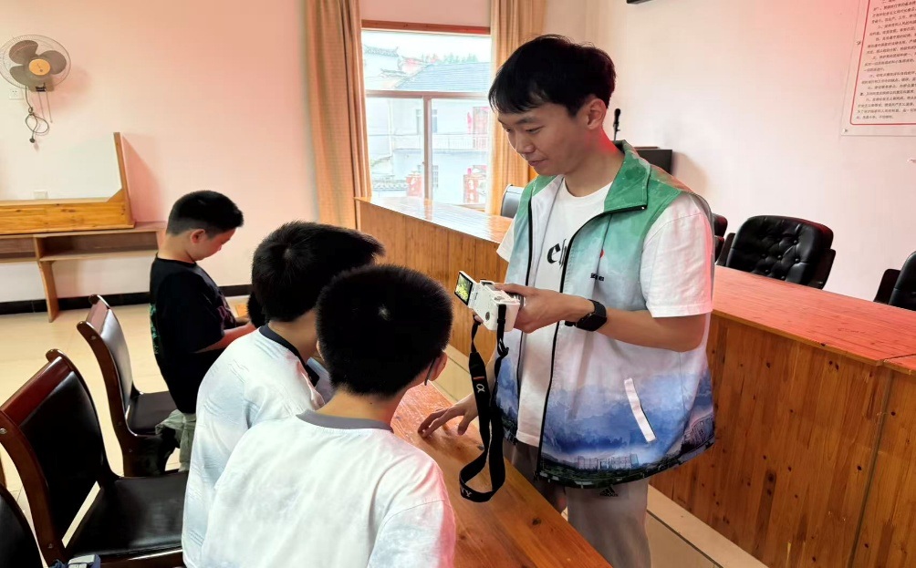 图为圆梦志愿支教队员手持相机,近距离向少年讲解相机操作要点,开展摄影实操教学。