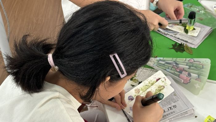 图为在草本拓印手工课上,上课孩子正在完成自己的植物拓印书签作品