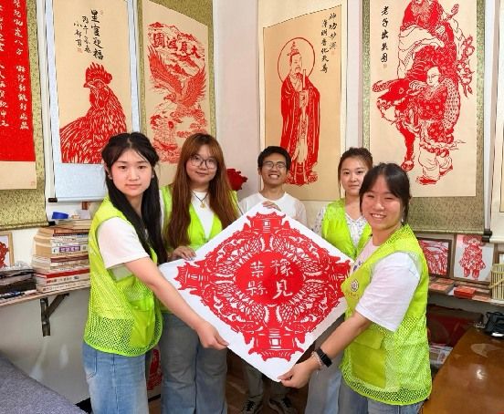 图为实践队员与剪纸非遗传承人都世奎共同展示刻有团队名称的剪纸作品。刘奕珂供图