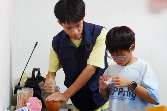 图为在草木香囊制作课上,义教组老师现场示范传统草药研磨技艺,带领小朋友体验非遗手工活动