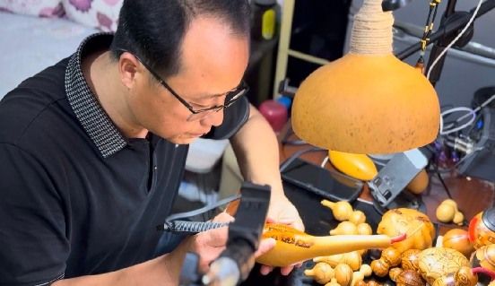 图为葫芦烙画非遗传承人周军辉向实践队员展示烙画制作过程。刘奕珂供图